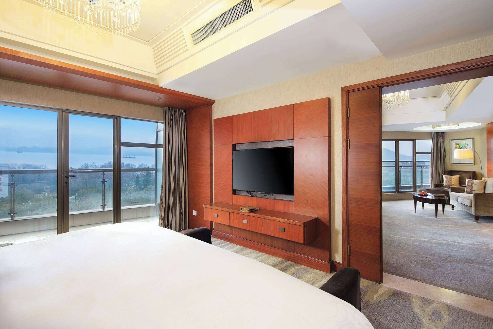 Une chambre d’hôtel dotée d’un grand lit, d’un téléviseur fixé au mur, d’un balcon avec vue et d’un espace de vie séparé comprenant un canapé et une table basse.