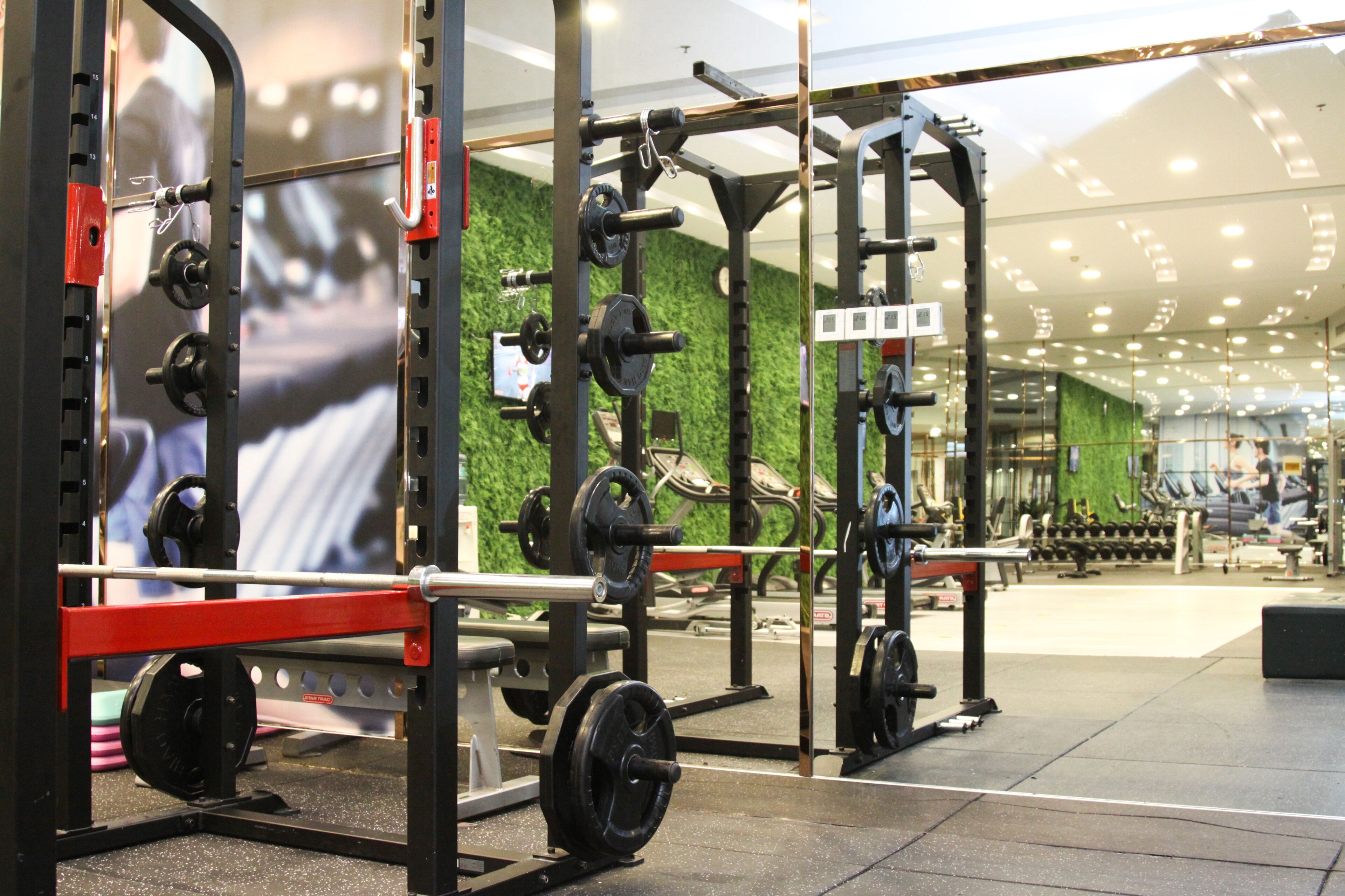Un gimnasio con equipo de levantamiento de pesas, una pared verde y un espejo que refleja el equipo.