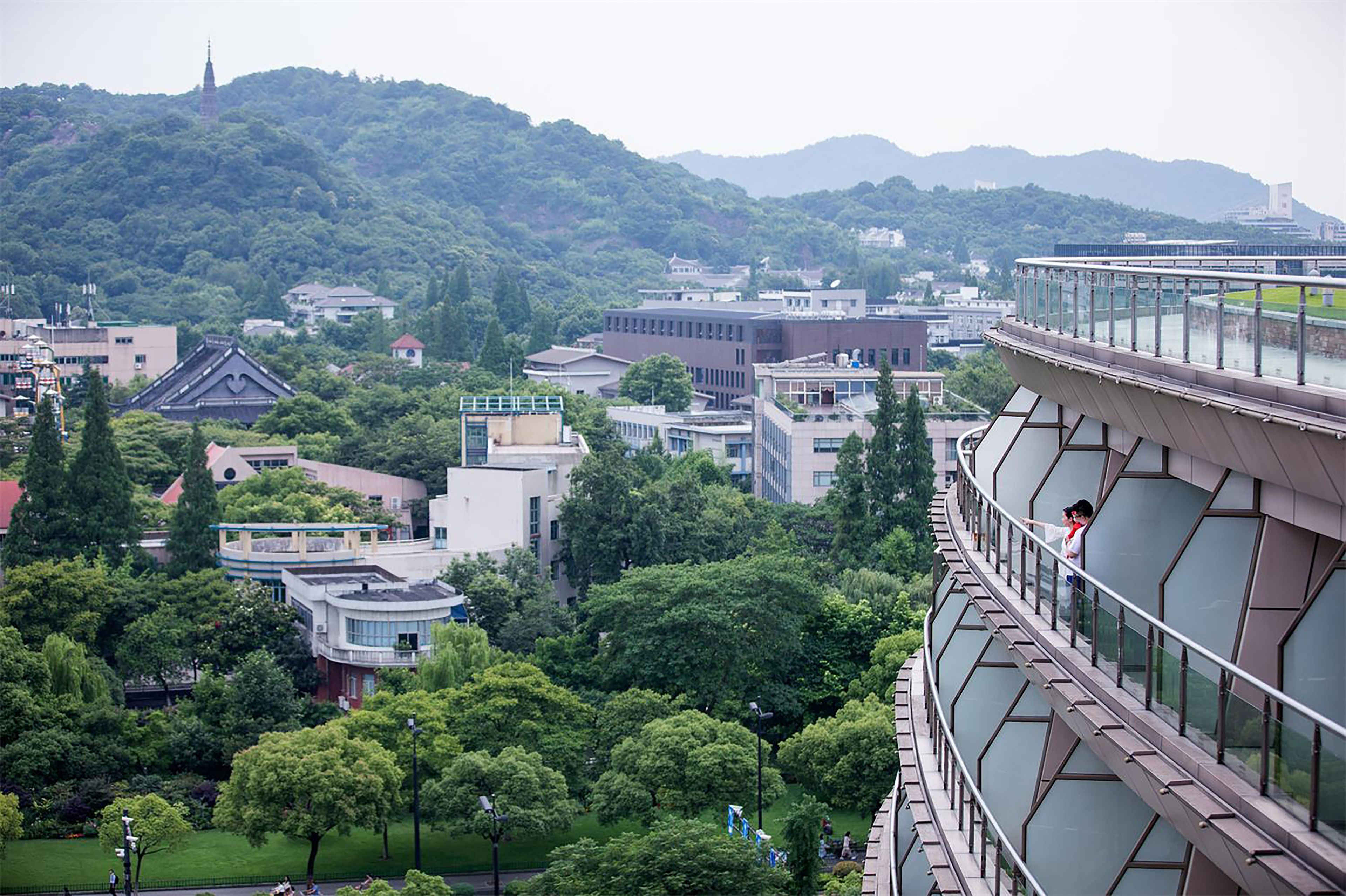 A modern building with a glass facade, surrounded by lush greenery and other buildings.