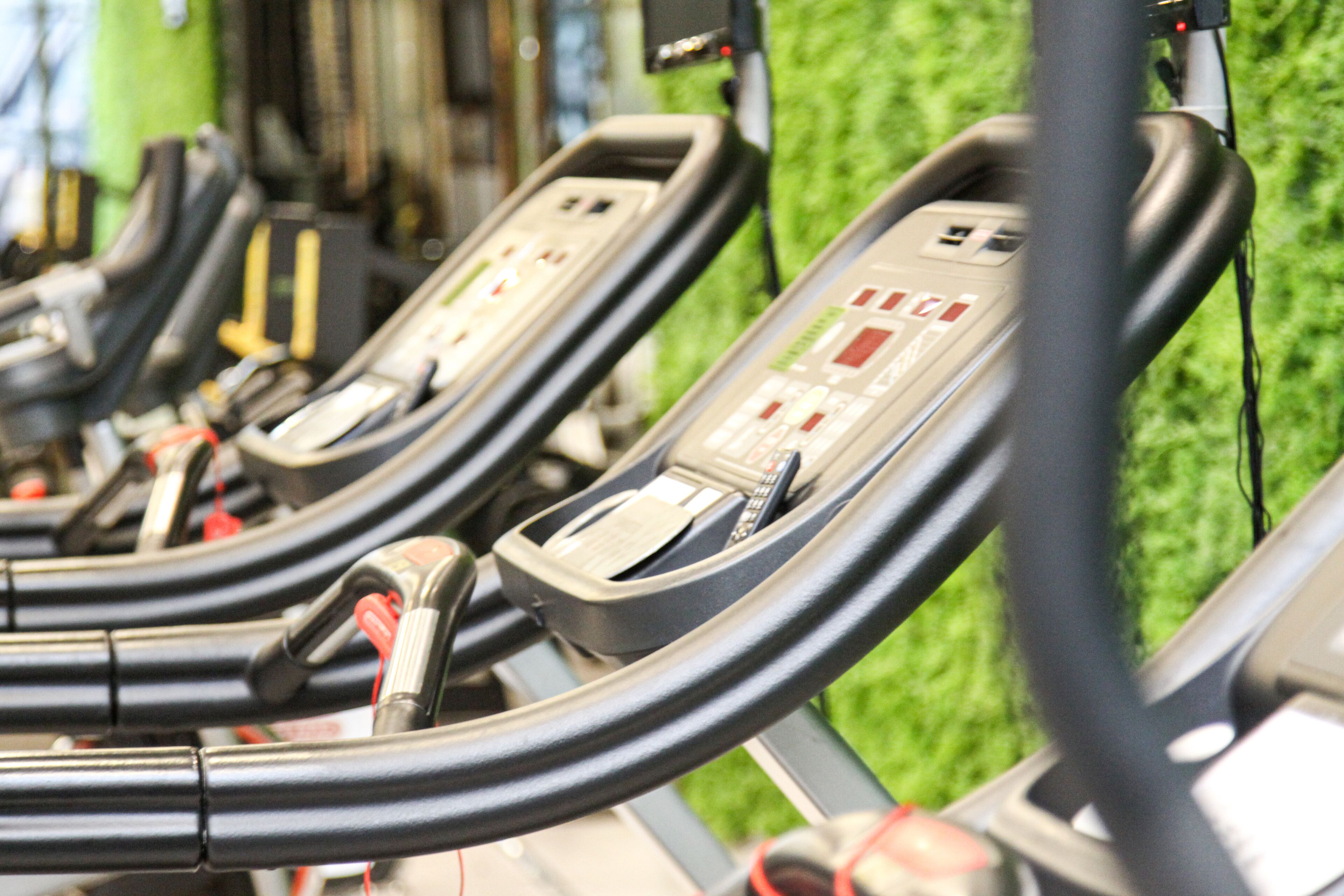 A row of stationary exercise bikes with control panels, set against a backdrop of artificial green turf.