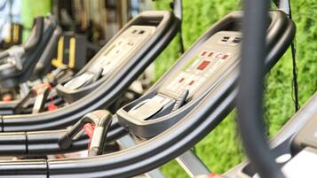 A row of stationary exercise bikes with control panels, set against a backdrop of artificial green turf.