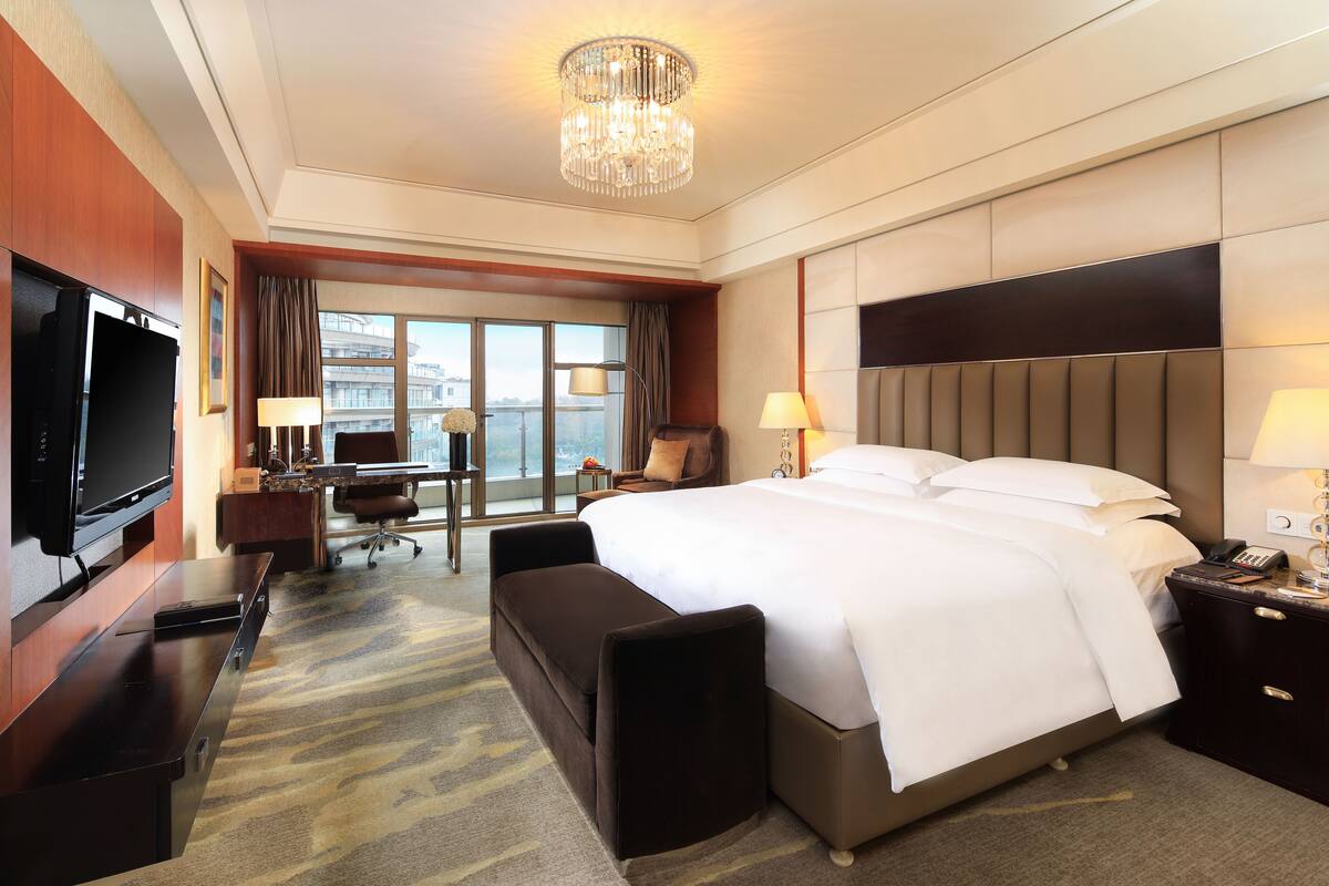 A hotel room with a large bed, a desk with a computer, a TV, and a view of the city.