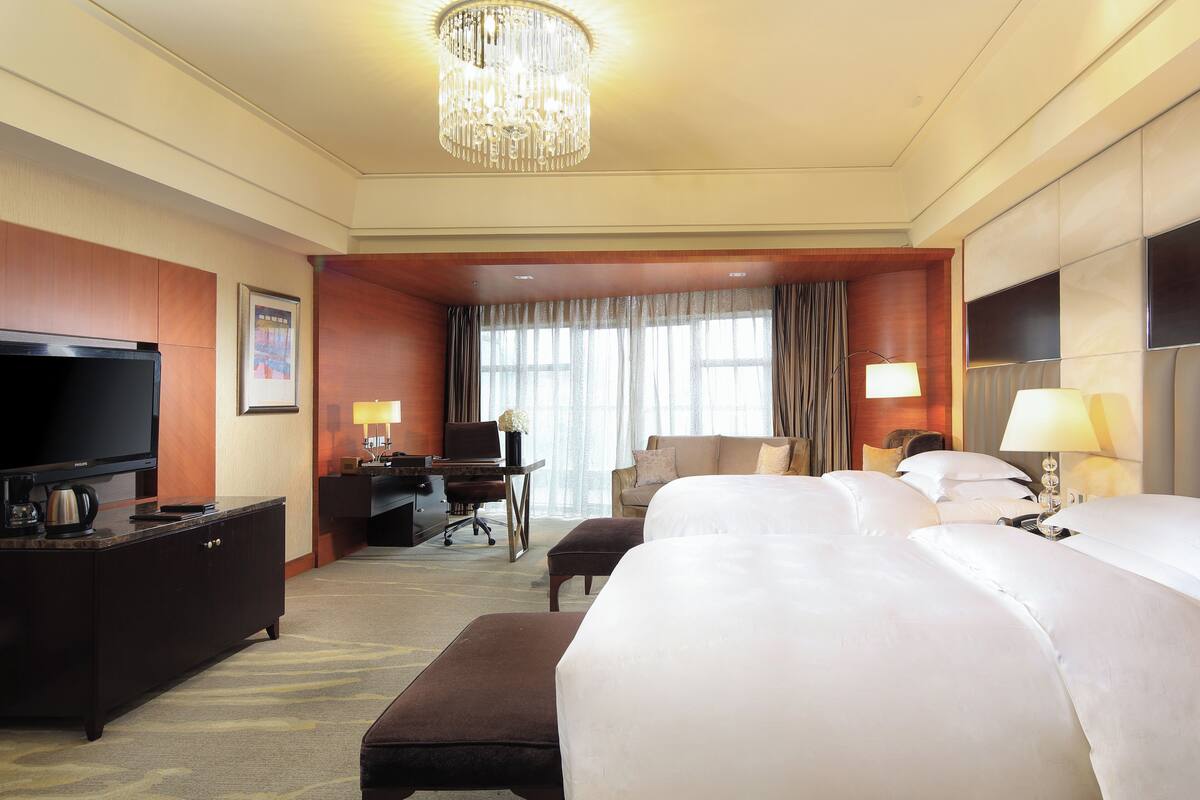 A hotel room with a large bed, a desk with a computer, a television, and a chandelier.