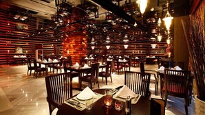 A restaurant with multiple dining tables and chairs, wooden panel walls, and hanging light fixtures.