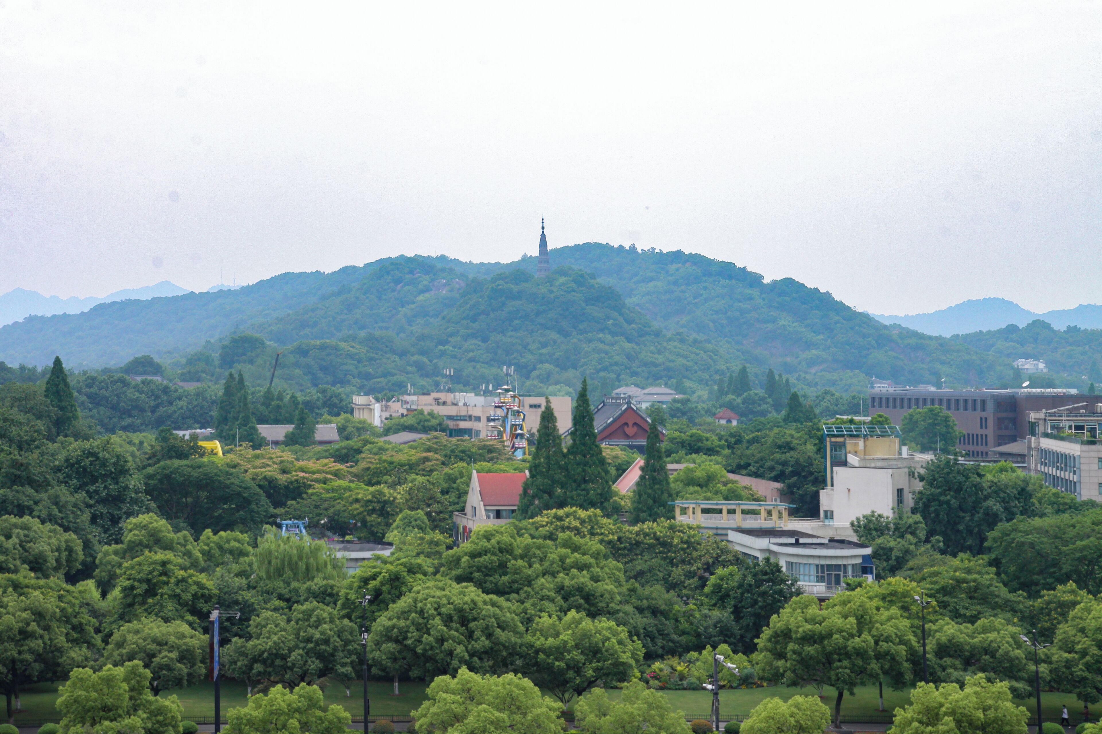 Un paisaje urbano con una torre destacada en una colina, rodeado de abundante vegetación y varios edificios.