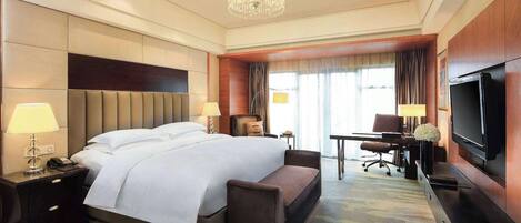 A hotel room with a large bed, a desk, a chair, a television, and a chandelier.