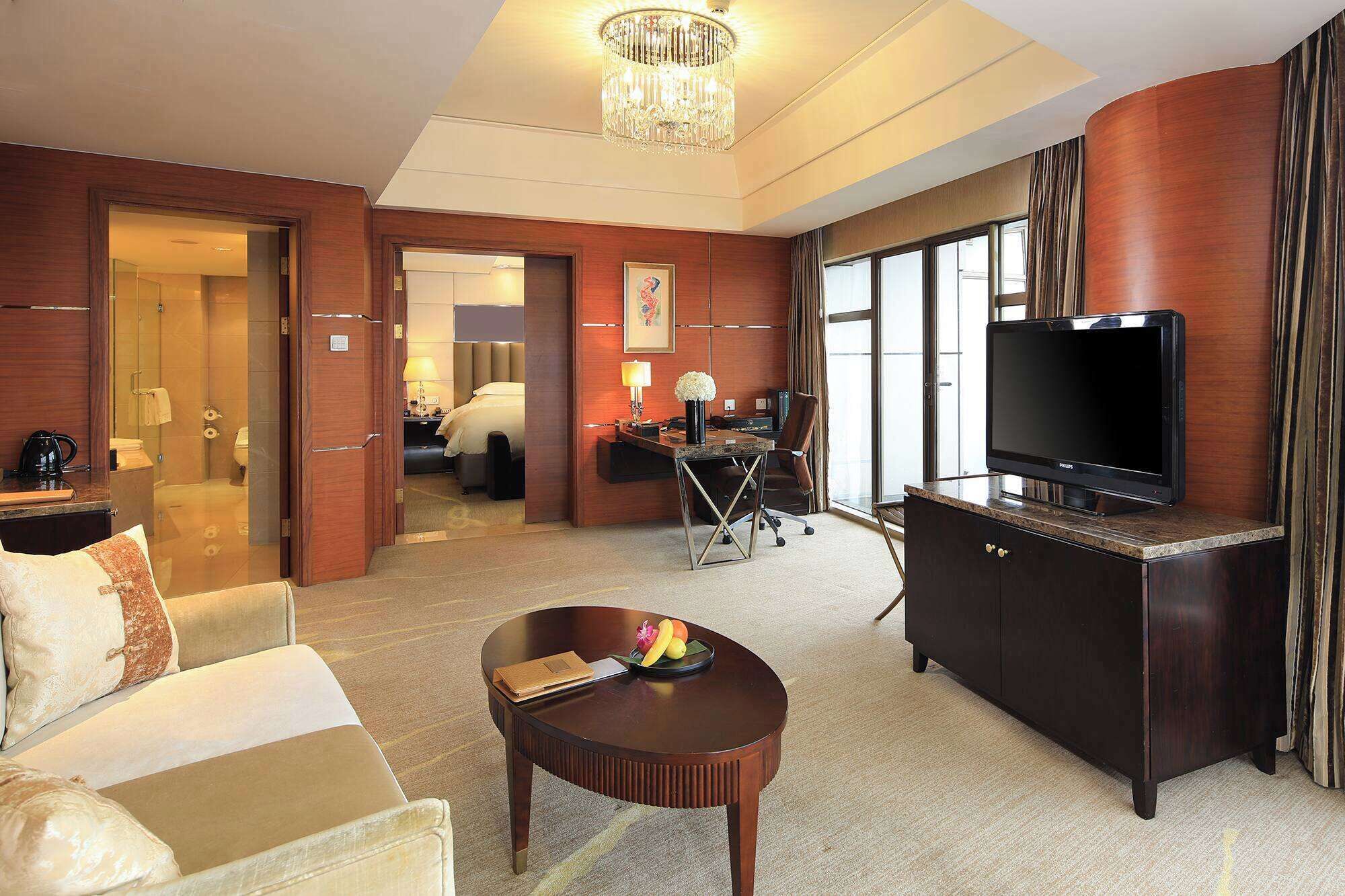 A hotel room with a large TV, a desk, a chair, a sofa, and a coffee table.