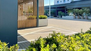 A modern building with a covered outdoor area, a paved walkway, and greenery. - Hotel Ilonn (Poznan)