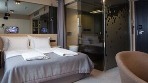A modern hotel room with a large bed, a small side table, a glass shower enclosure, and a dark door. - Hotel Ilonn (Poznan)