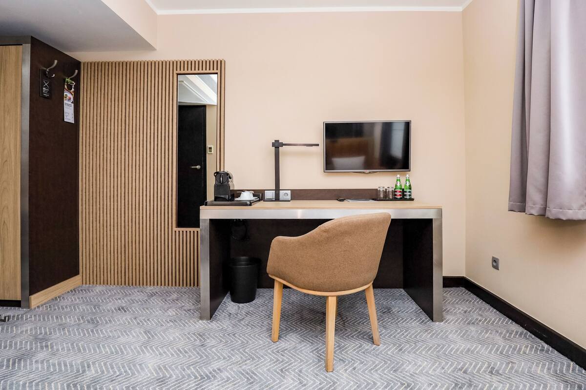 A hotel room with a desk, chair, television, and a mirror.