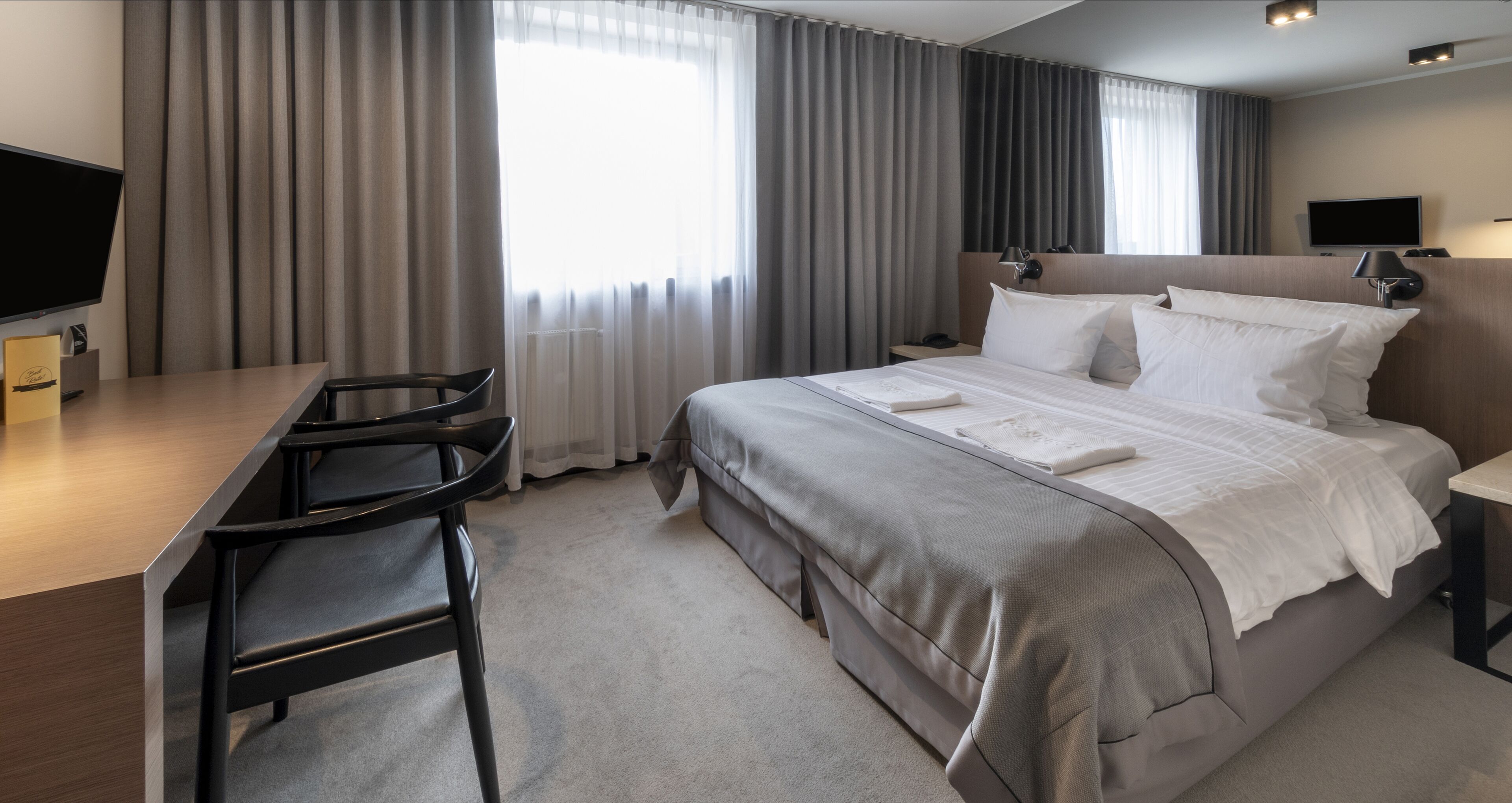A hotel room with a bed, a desk, a chair, a TV, and a window with curtains.