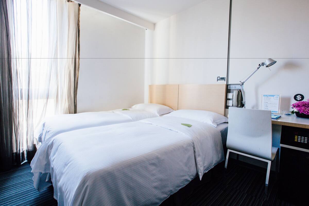 A hotel room with two beds, a desk with a lamp, and a view of the outdoors.
