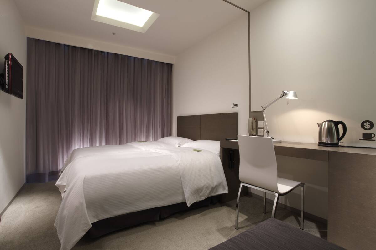 A hotel room with a bed, a desk, a chair, a desk lamp, and a coffee maker.