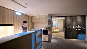 A modern reception area with a reception desk, a digital clock displaying the time, and a wall with a café sign. - Just Sleep Taipei Linsen (Taipei)