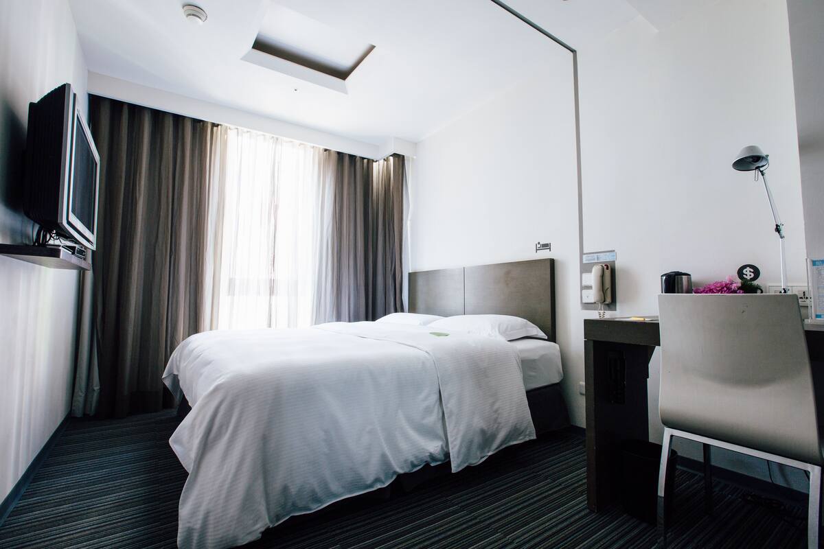 A hotel room with a bed, a desk, a chair, a television, and a window with curtains.