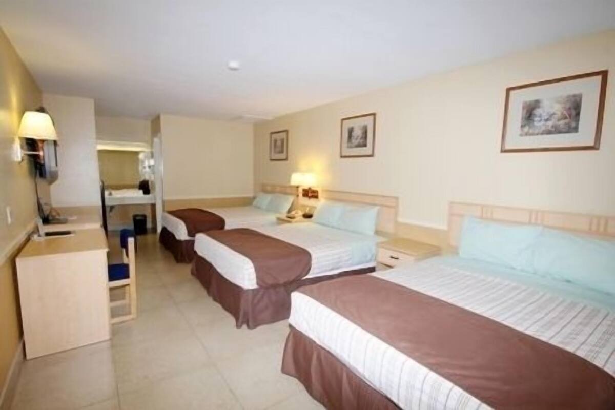 Habitación de hotel con tres camas, un escritorio y un espejo.
