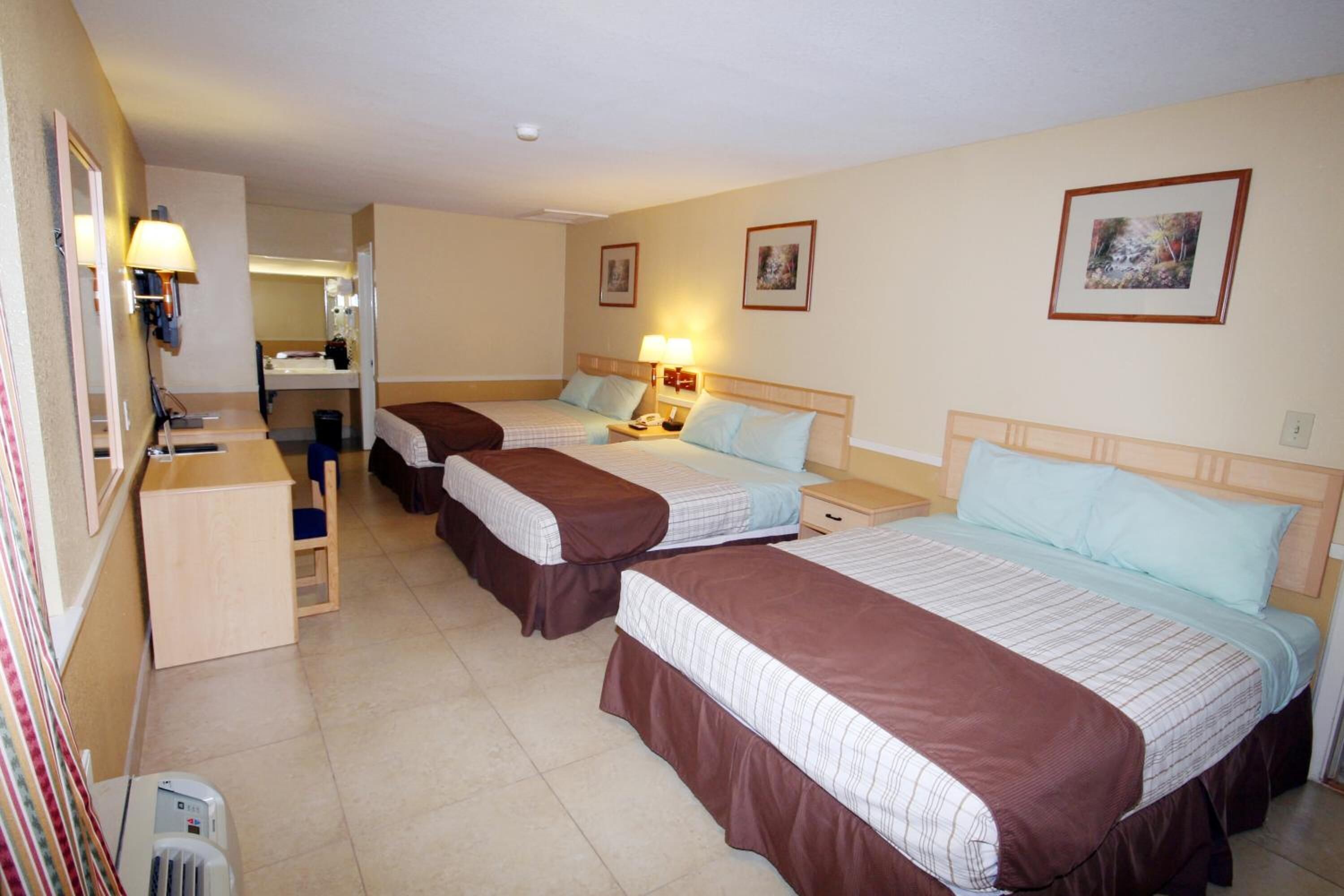 Habitación de hotel con tres camas, un escritorio, un espejo y un baño pequeño.