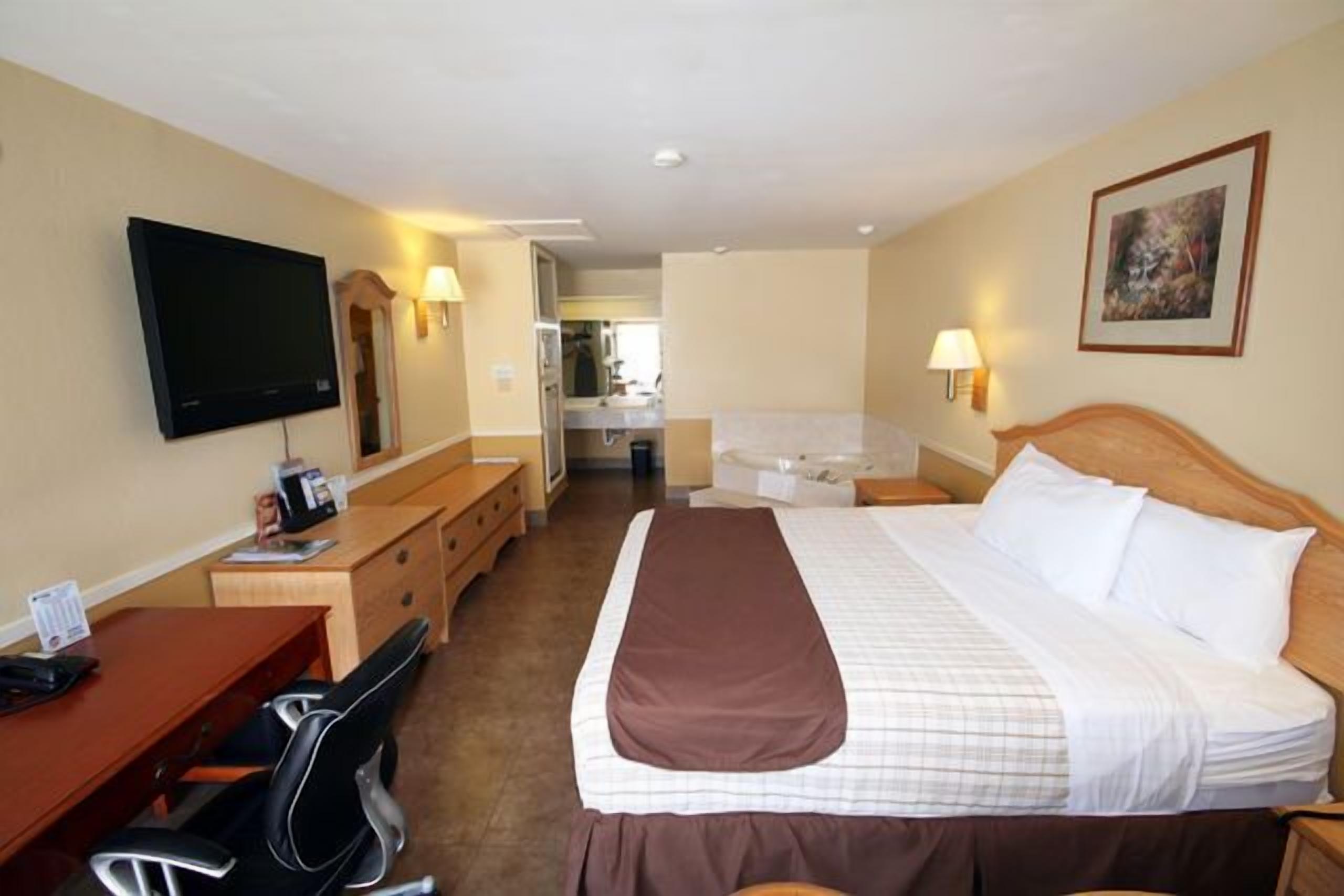 A hotel room with a bed, a desk with a chair, a television, and a bathroom visible through an open door.