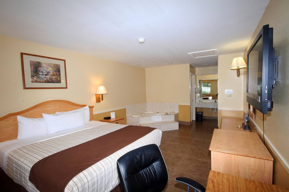 Habitación de hotel con una cama grande, un escritorio, un televisor, un baño y un cuadro en la pared.