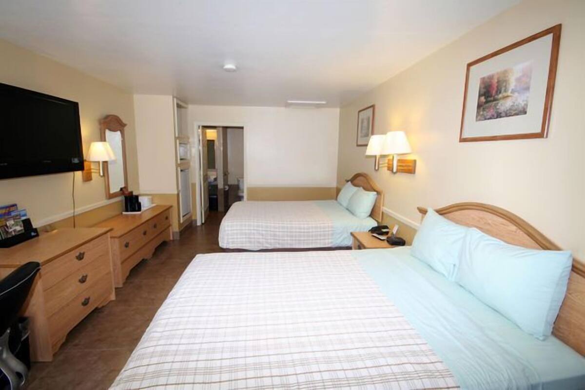Habitación de hotel con dos camas, un escritorio, un televisor y una puerta que da a un baño.