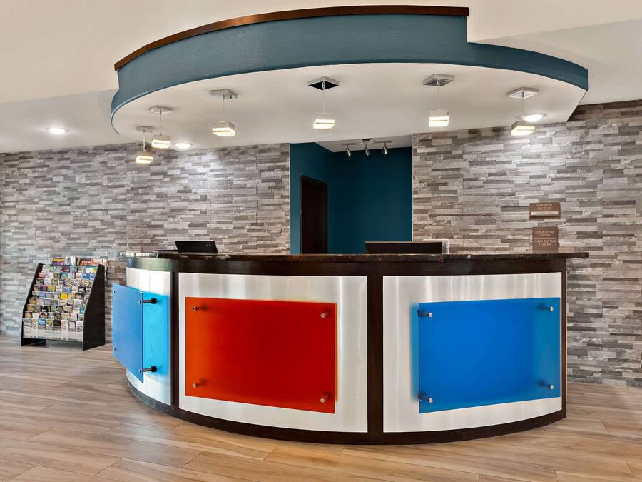 Un mostrador de recepción con diseño curvo, una combinación de colores azul y rojo, y un cartel en la pared que indica los horarios de registro.
