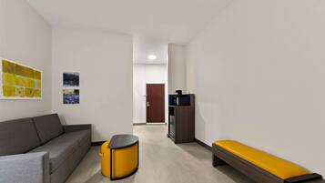 Una sala de estar moderna con un sofá gris, una mesita auxiliar amarilla, un banco de madera y un televisor sobre un mueble de madera.