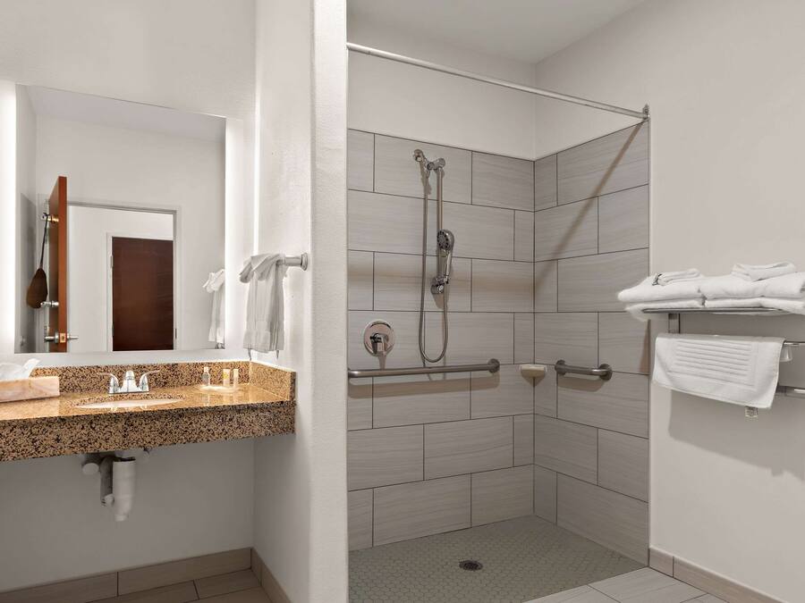 Une salle de bain moderne avec un comptoir en granit, une douche équipée d’un pommeau de douche à main et un porte-serviettes où sont pliées les serviettes.