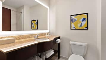 A modern bathroom with a large mirror, a sink, a toilet, and two framed artworks on the wall.
