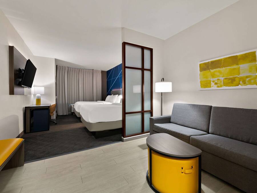 A modern hotel room with a bed, a sofa, a small table, a TV, and a painting on the wall.