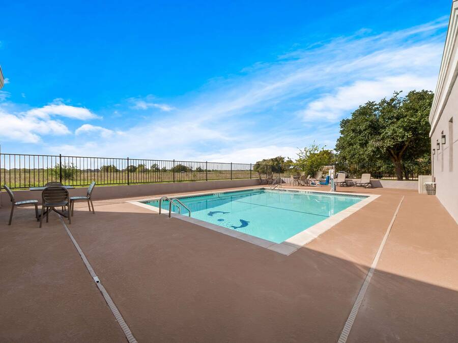 A rectangular pool with a metal ladder, surrounded by a concrete deck. There are lounge chairs and a table with chairs on the deck.