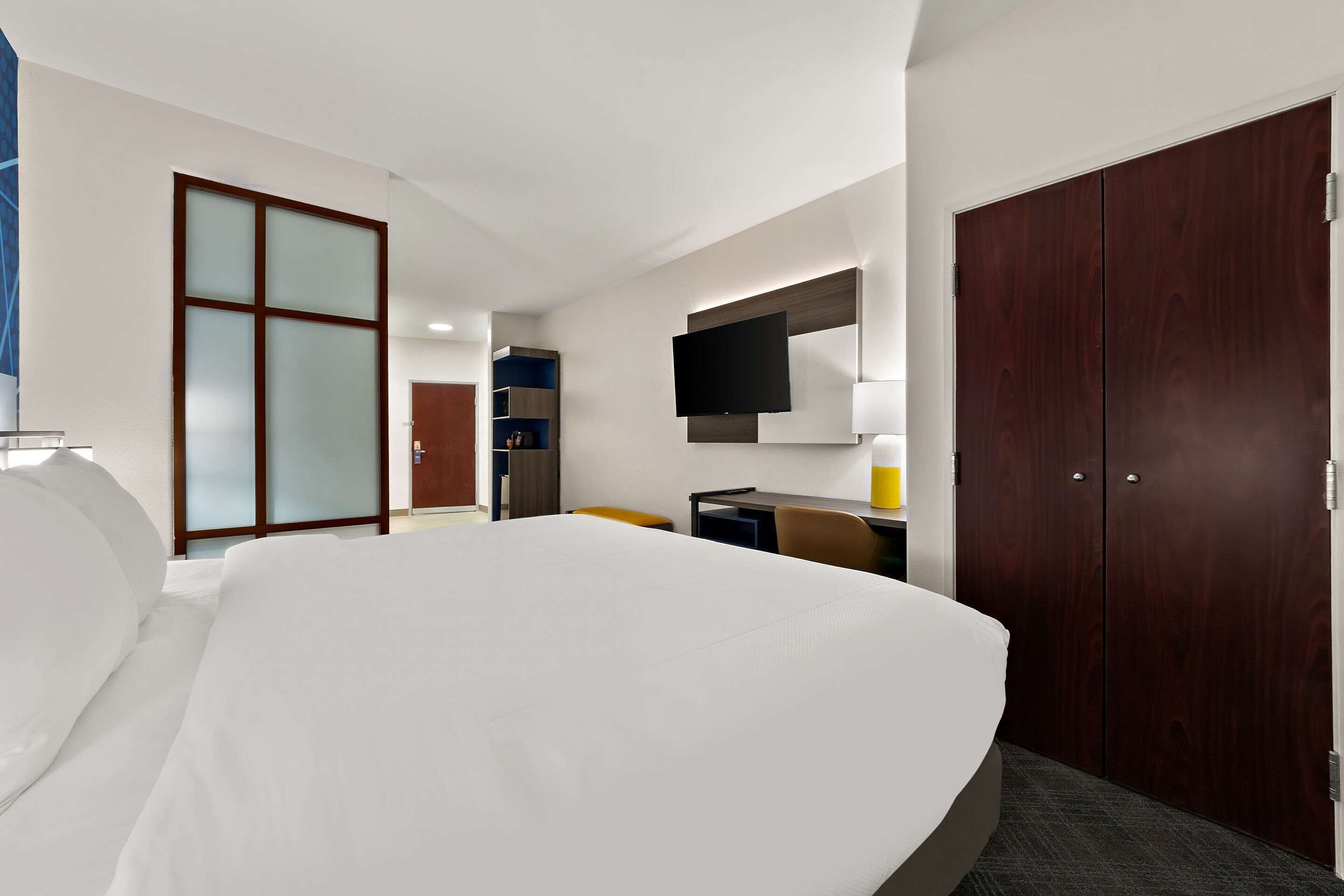 Ein Hotelzimmer mit einem großen Bett, einem Schreibtisch mit Stuhl, einem an der Wand montierten Fernseher und einem Kleiderschrank.