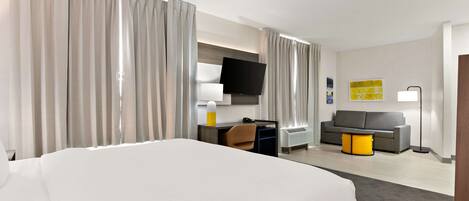 A hotel room with a large bed, a desk with a chair, a sofa, a TV, and a lamp.