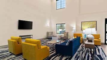 Een moderne hotellobby met gele fauteuils, een blauwe bank, een flatscreen televisie aan de muur en een kamerbreed tapijt met dessin.