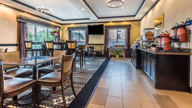 A hotel dining area with a long counter, multiple seating arrangements, and a television screen. - Days Inn & Suites by Wyndham Mineral Wells (Mineral Wells)