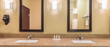 A hotel bathroom with two sinks, two mirrors, and a hairdryer on the wall.