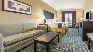 A hotel room with a sofa, a bed, a desk, and a television. - Days Inn & Suites by Wyndham Mineral Wells (Mineral Wells)