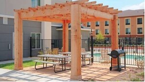 An outdoor patio area with a wooden pergola, picnic tables, and a barbecue grill. - Days Inn & Suites by Wyndham Mineral Wells (Mineral Wells)