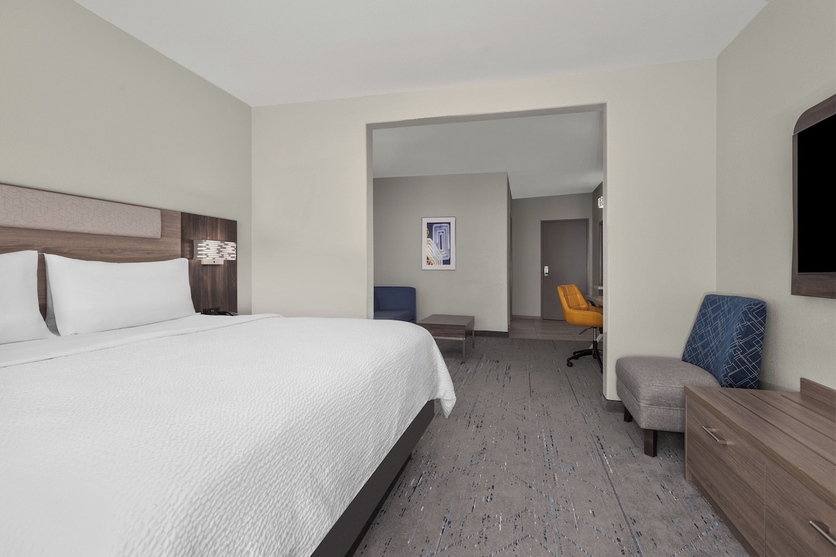 A hotel room with a large bed, a desk, a chair, and a television.