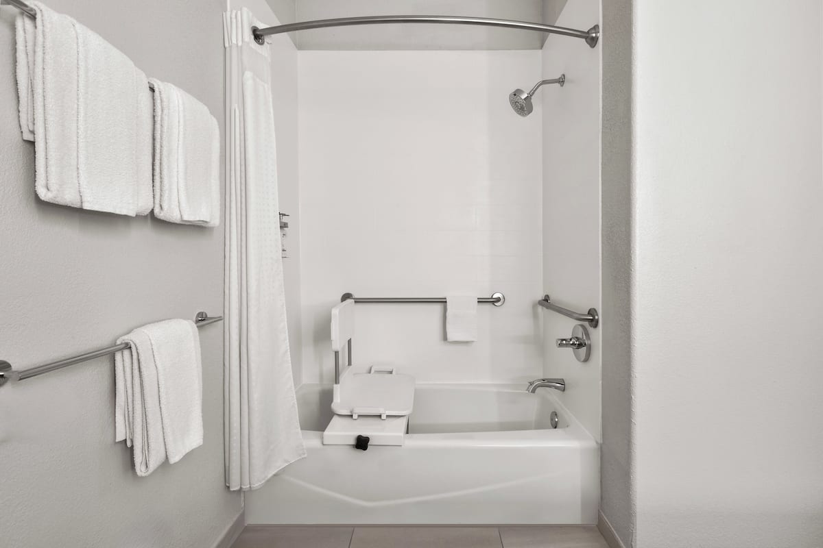 A modern bathroom with a walk-in shower, grab bars, a white bathtub, and a towel rack.