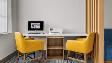 A hotel room with a white desk, two yellow chairs, a computer, and a printer.