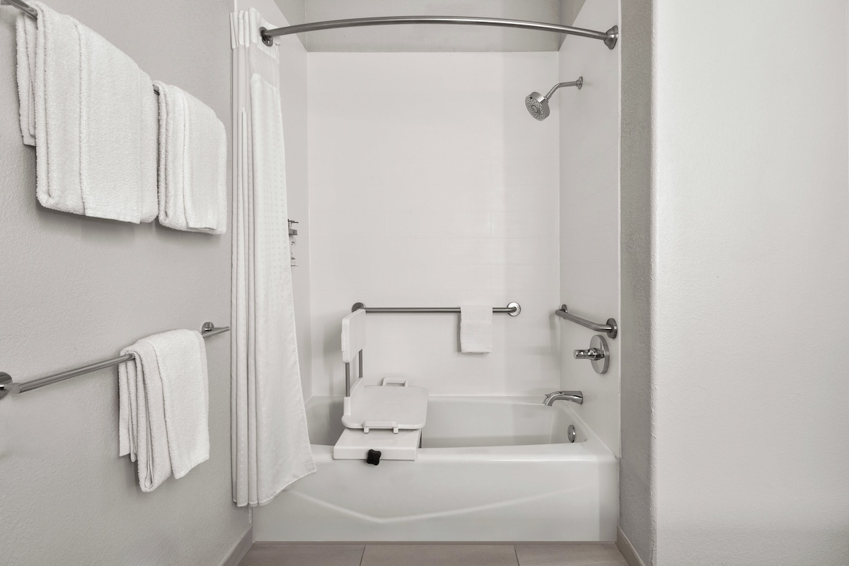 A modern bathroom with a walk-in shower, grab bars, a white bathtub, and a towel rack.