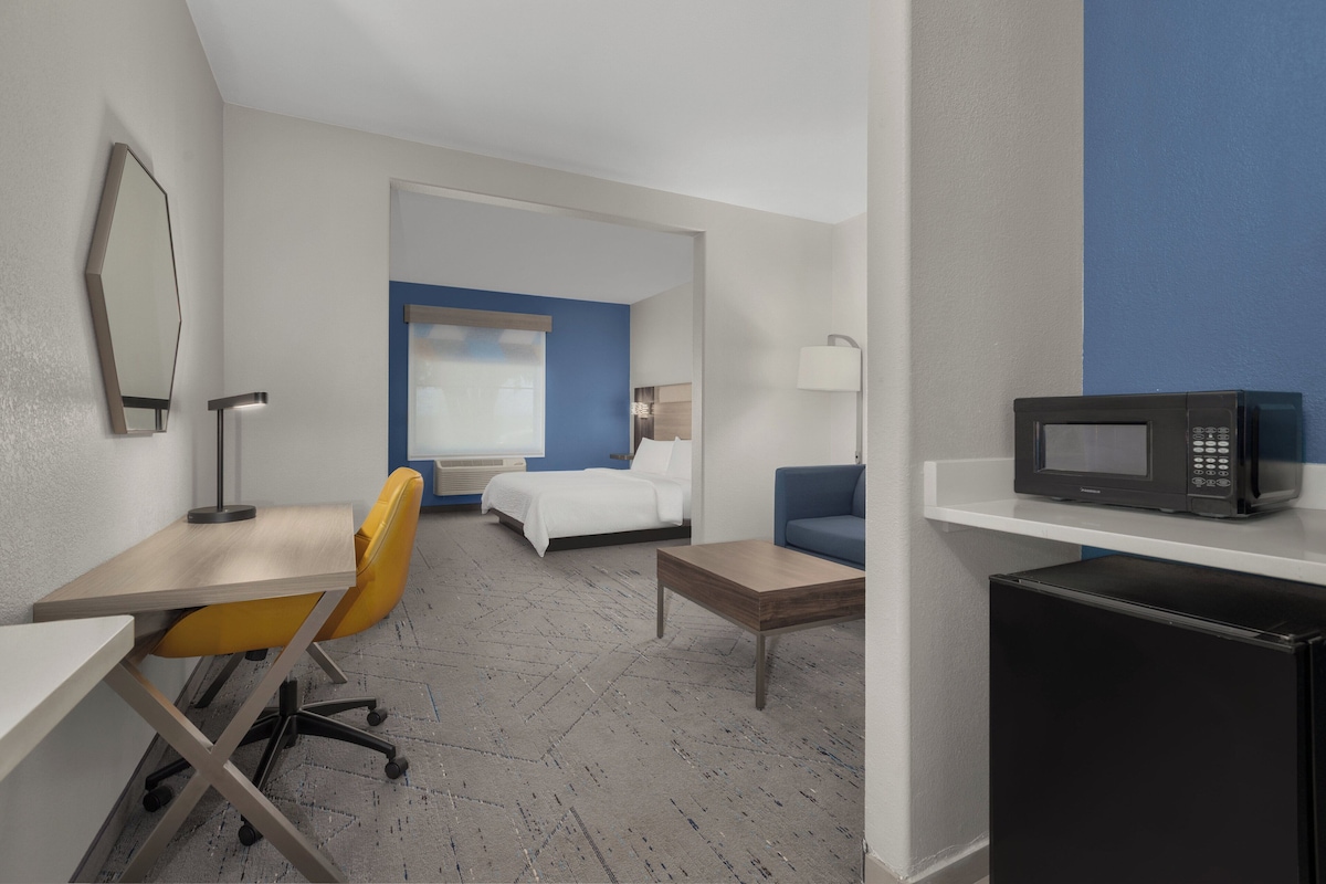 A hotel room with a bed, desk, chair, microwave, and a small refrigerator.