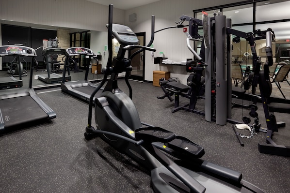 Un gimnasio con cintas de correr, elípticas y equipo de levantamiento de pesas.