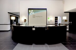 Recepção com uma grande tela exibindo o nome do hotel, um balcão e um homem atrás dele.