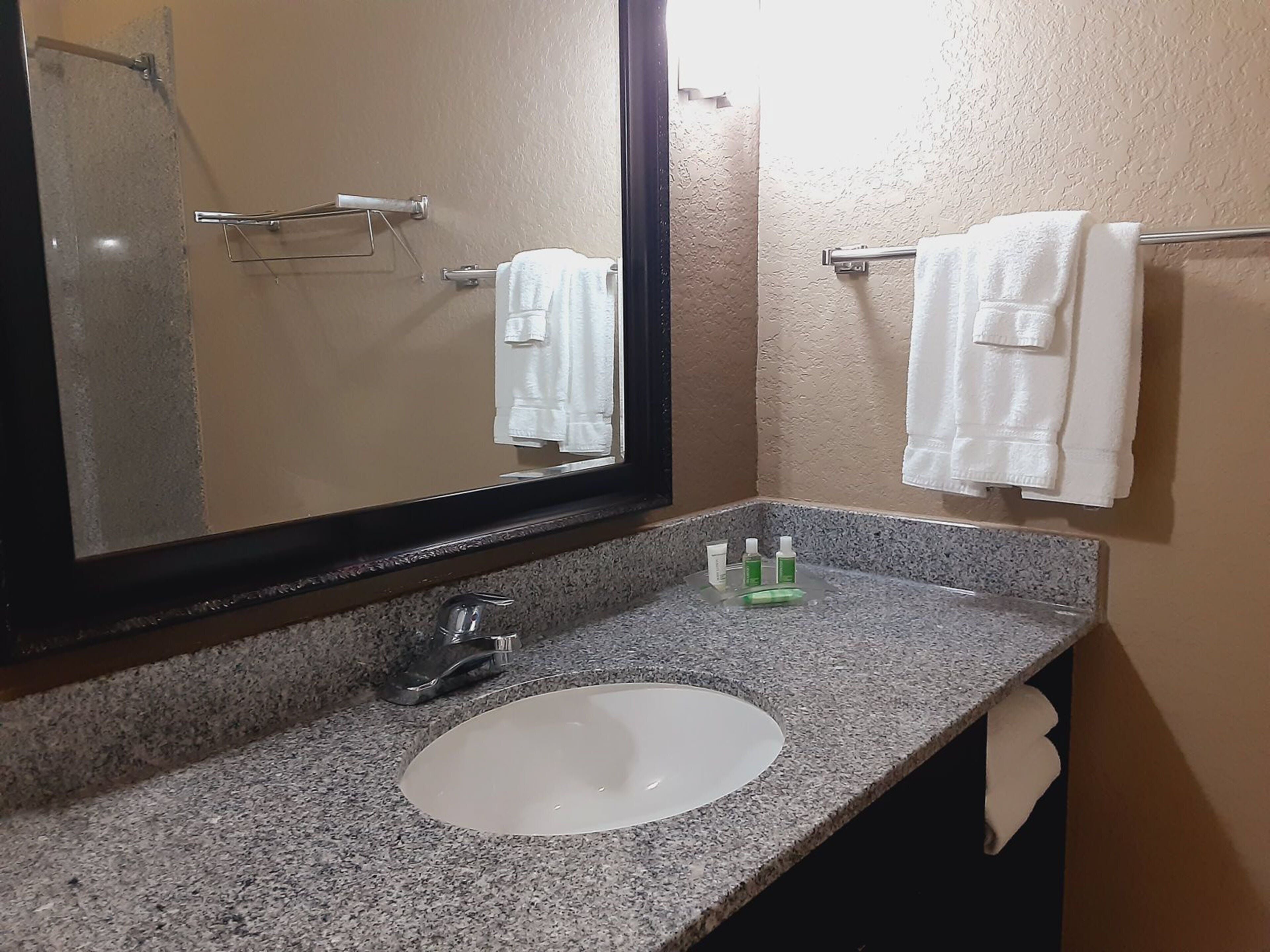 Un baño con encimera de granito, un lavabo blanco, un espejo y dos toallas colgadas en barras.