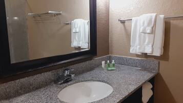Un baño con encimera de granito, un lavabo blanco, un espejo y dos toallas colgadas en barras.