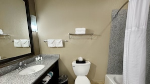 Un baño con encimera de granito, dos lavamanos, inodoro, cortina de ducha y toalleros.