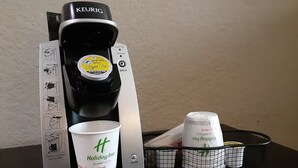 Una cafetera Keurig con un cápsula de Royal Cup, una taza desechable y una taza reutilizable con el logo de Holiday Inn.