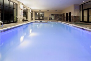 Ein hallenbad mit klarem Wasser, einer Rettungswache und einer Sitzgelegenheit mit Stühlen.