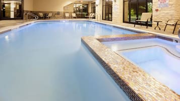 A swimming pool with a tiled edge, a lifeguard warning sign, and outdoor seating.